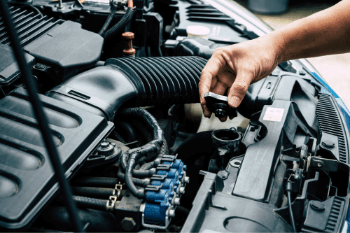 Factory recommended vehicle maintenance in Parkton, NC. with Brian's Motor Werks. Image of mechanic hand holding the radiator cap from vehicle while checking coolant on car in shop.